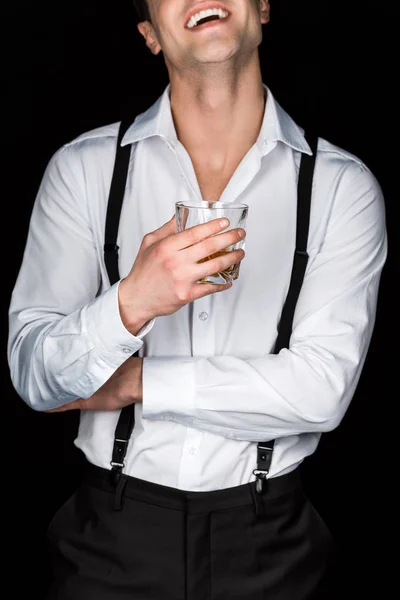 Vue recadrée de l'homme heureux en chemise blanche et bretelles tenant verre de whisky isolé sur noir — Photo de stock