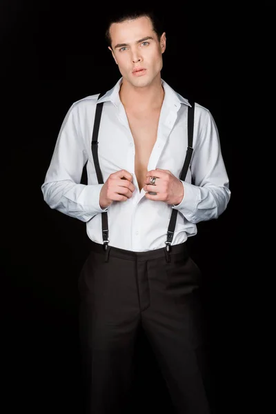 Schöner Mann steht und berührt weißes Hemd isoliert auf schwarz — Stockfoto