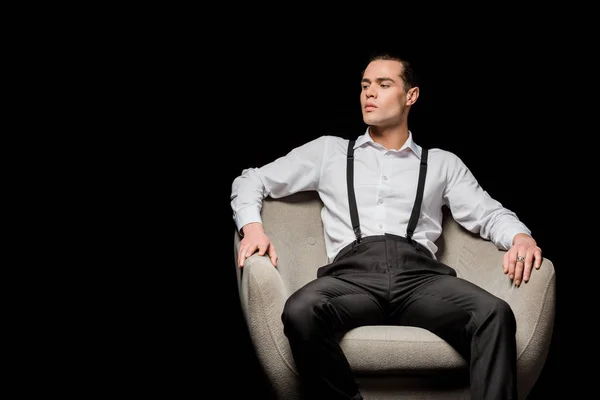 Bel homme en chemise assis dans un fauteuil isolé sur noir — Photo de stock