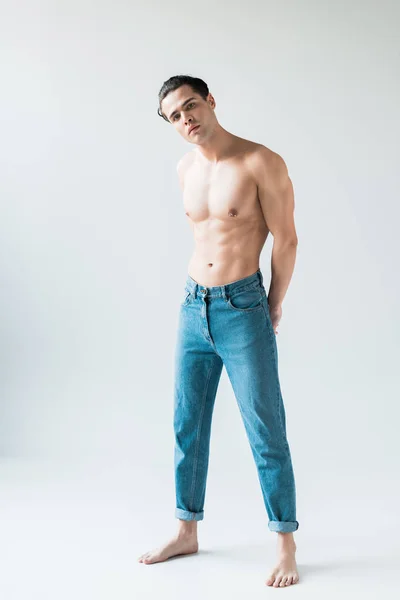 Красивий без сорочки чоловік стоїть у блакитних джинсах і дивиться на камеру на білому — стокове фото