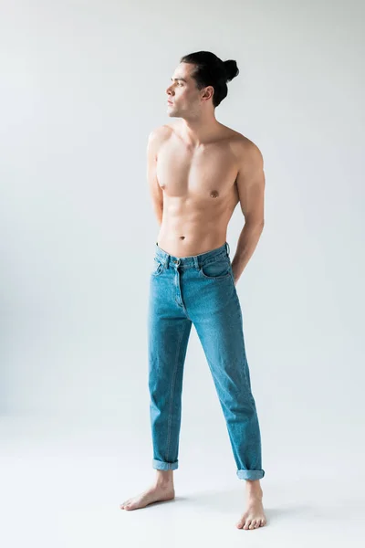 Schöner hemdloser Mann, der in blauen Jeans auf weißem Grund steht — Stockfoto