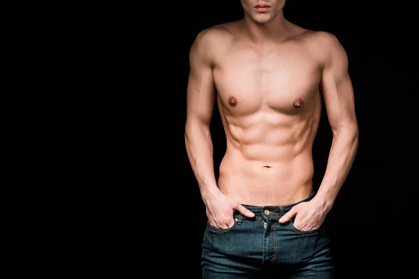 Cropped view of serious and shirtless man standing with hands in pockets isolated on black — Stock Photo