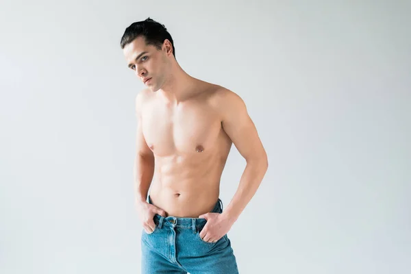 Bell'uomo senza camicia in piedi in jeans blu con le mani in tasca su bianco — Foto stock
