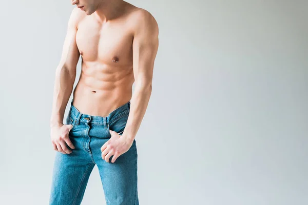 Обрізаний вид м'язистого і без сорочки чоловіка в джинсах, що стоять на білому — стокове фото