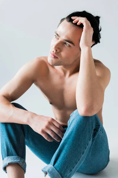 Hombre pensativo y sin camisa sentado en pantalones vaqueros azules en blanco - foto de stock