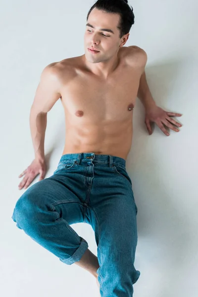 Overhead view of muscular and shirtless man lying in blue jeans on white — Stock Photo