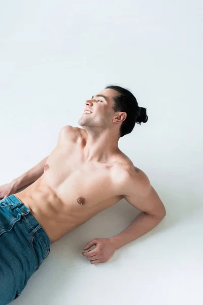 Overhead view of cheerful muscular man lying in blue jeans on white — Stock Photo
