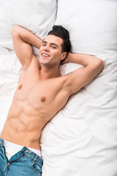 Overhead view of happy shirtless man smiling while lying on bed — Stock Photo