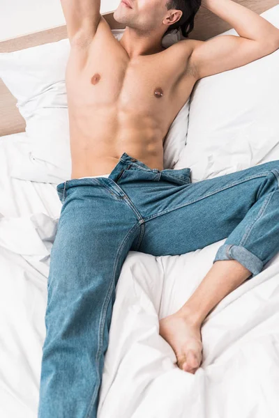 Обрезанный вид человека без рубашки в джинсах лежащего на кровати дома — стоковое фото