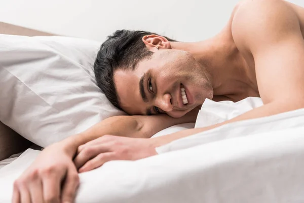 Vista de ángulo bajo del hombre feliz mirando a la cámara mientras está acostado en la cama - foto de stock