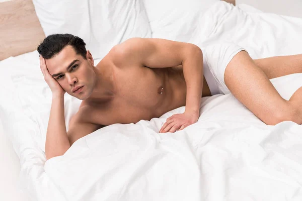 Schöner muskulöser Mann, der in die Kamera schaut und auf dem Bett liegt — Stockfoto