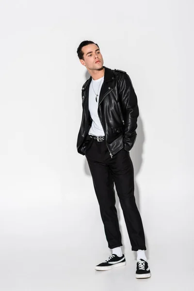 Handsome man in leather jacket standing with hands in pockets on white — Stock Photo