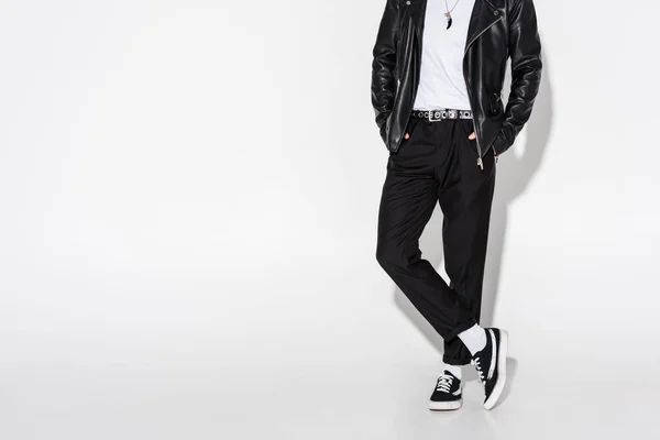 Cropped view of man in leather jacket standing with crossed legs on white — Stock Photo