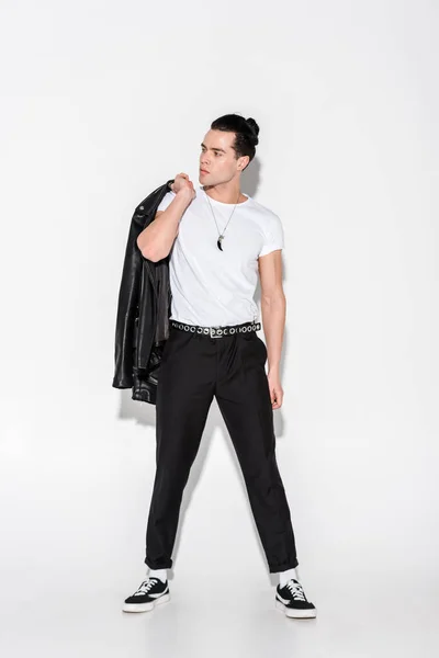 Handsome man in white t-shirt holding leather jacket while standing on white — Stock Photo