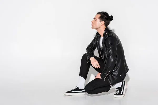 Handsome man in black leather jacket sitting on white — Stock Photo