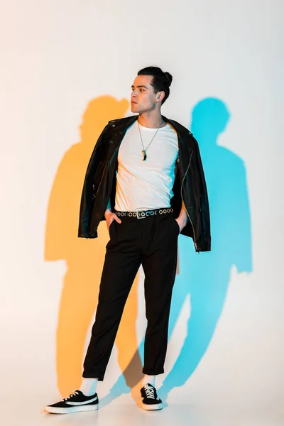 Красивый мужчина в черной кожаной куртке, стоящий с руками в карманах на белом с подсветкой — стоковое фото