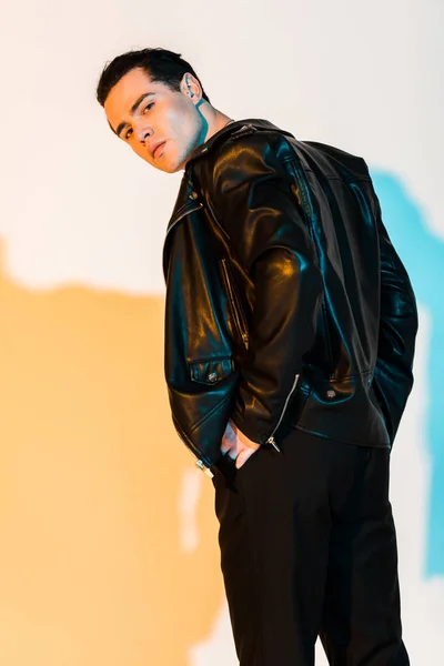 Homem bonito em jaqueta de couro preto de pé e olhando para a câmera no branco com iluminação — Fotografia de Stock