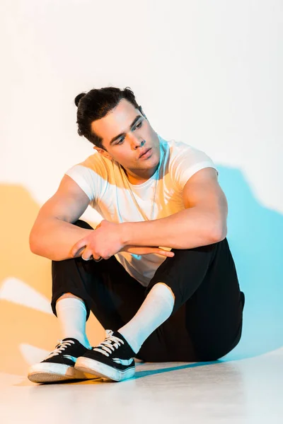 Pensive man in white t-shirt sitting on white with illumination — Stock Photo