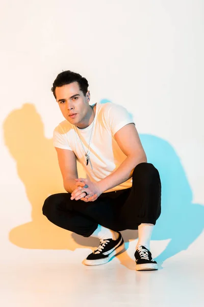 Schöner Mann in weißem T-Shirt sitzt mit geballten Händen auf weißem mit Beleuchtung — Stockfoto