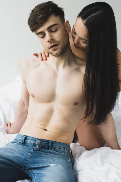 Hermosa asiático mujer abrazando sin camisa novio en dormitorio - foto de stock