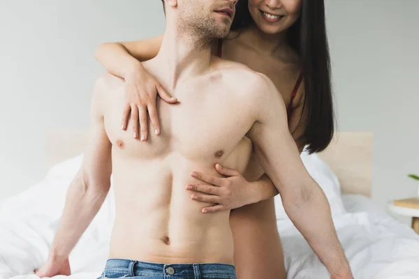 Vista recortada de la mujer sonriente abrazando novio sin camisa en el dormitorio - foto de stock