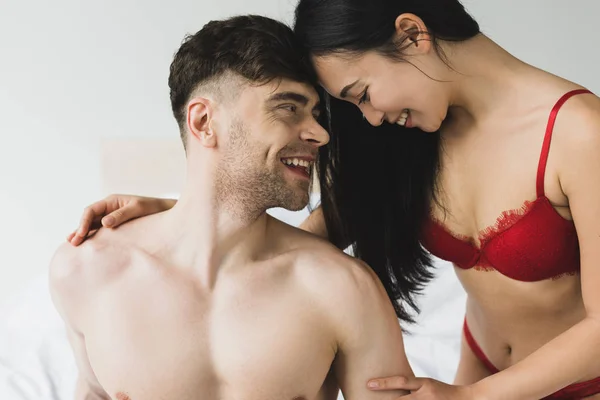 Веселая межрасовая пара улыбается и смотрит друг на друга в спальне — стоковое фото