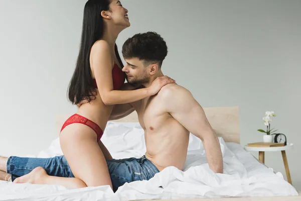 Alegre asiático mujer abrazando con guapo novio en dormitorio - foto de stock