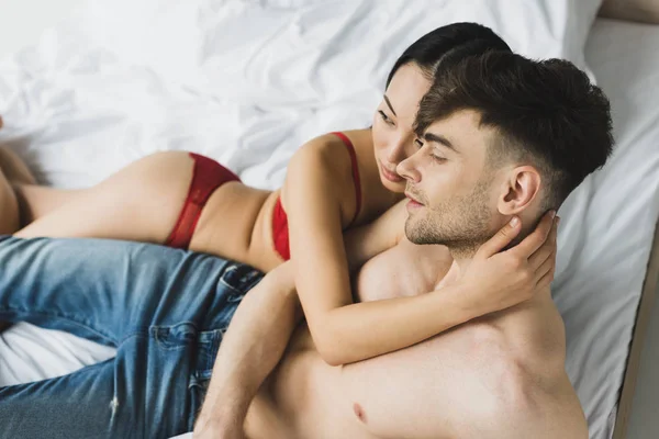 Young interracial couple embracing and looking away while lying on bed — Stock Photo