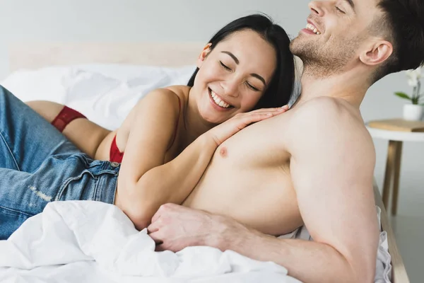 Cheerful asian woman lying on chest of happy shirtless boyfriend — Stock Photo