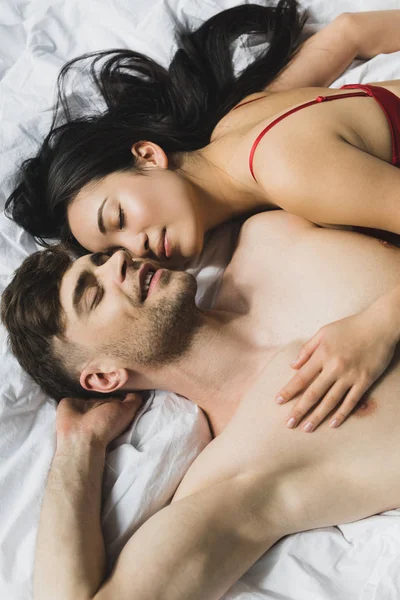 Vue de dessus de couple interracial aimant couché sur la literie blanche avec les yeux fermés — Photo de stock