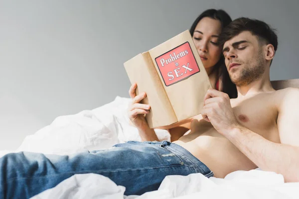 Junges interrassisches Paar liest Probleme in Sexbuch, während es zusammen im Bett liegt — Stockfoto