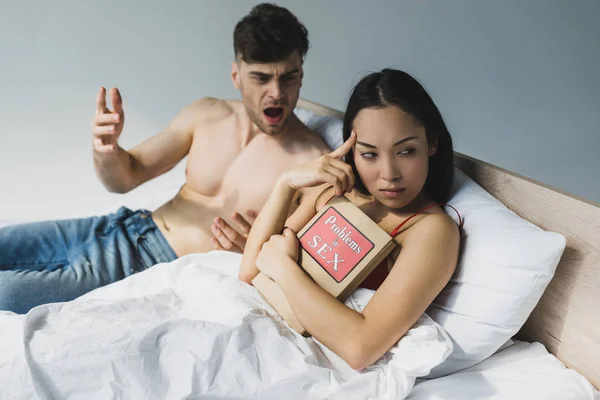 Foyer sélectif de offensé asiatique femme tenant des problèmes dans le livre de sexe tout en étant couché près de querelles copain — Photo de stock
