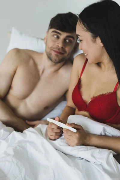 Selective focus of smiling woman holding pregnancy test near happy boyfriend — Stock Photo