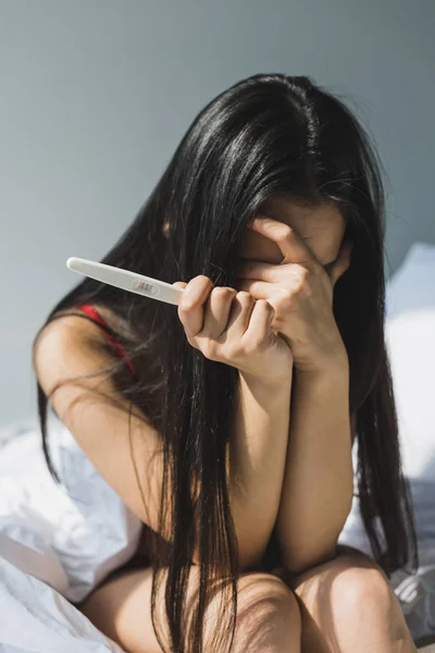 Upset asian woman holding pregnancy test and covering face with hand — Stock Photo