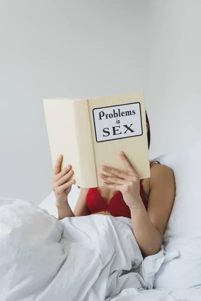 Young woman in red bra reading problems in sex book while lying in bed — Stock Photo