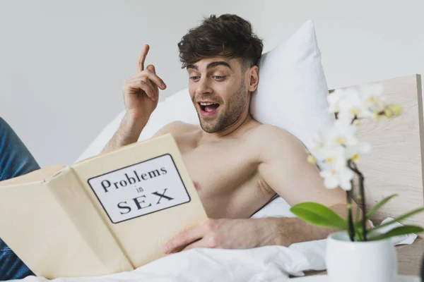 Smiling man showing idea sign while reading problems in sex book — Stock Photo