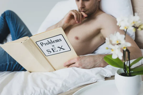 Вибірковий фокус без сорочки чоловіка, який читає проблеми в секс-книзі, лежачи в ліжку — стокове фото