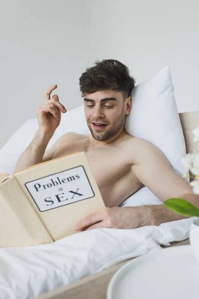 Cheerful man showing idea sign while reading problems in sex book — Stock Photo