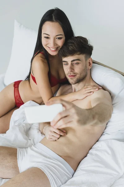 Selective focus of loving interracial couple in underwear taking selfie with smartphone — Stock Photo