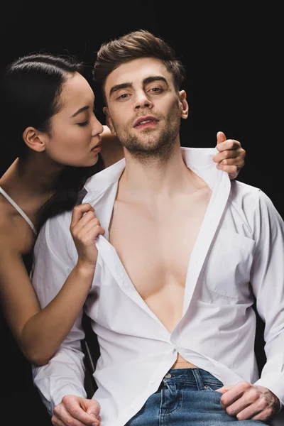 Sexy asian woman undressing handsome boyfriend isolated on black — Stock Photo