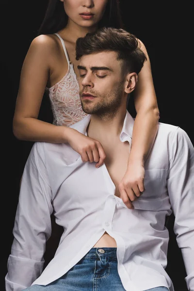 Cropped view of woman in white lingerie undressing handsome boyfriend isolated on black — Stock Photo