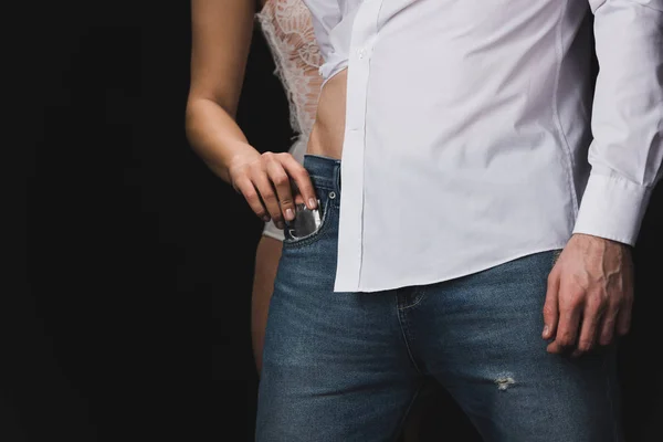 Corte vista de mulher ficando preservativo fora de namorados jeans bolso isolado no preto — Fotografia de Stock