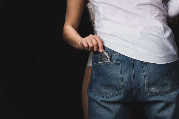 Cropped view of woman getting condom out of boyfriends jeans pocket isolated on black — Stock Photo