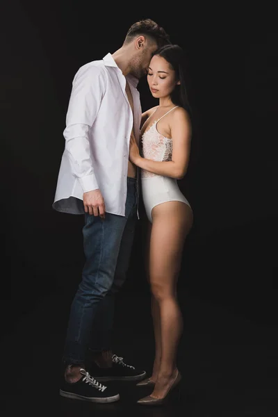 Sexy asian woman in white lingerie standing near boyfriend isolated on black — Stock Photo