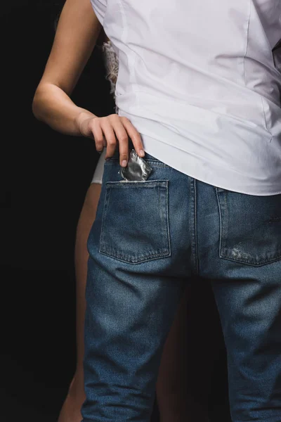 Corte vista de mulher ficando preservativo fora de namorados jeans bolso isolado no preto — Fotografia de Stock