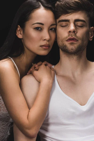 Attractive asian woman lying on shoulder of handsome boyfriend and looking at camera isolated on black — Stock Photo