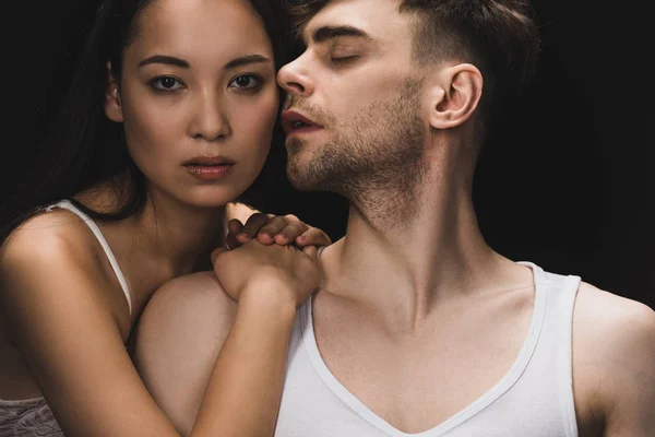 Attractive asian woman lying on shoulder of handsome boyfriend and looking at camera isolated on black — Stock Photo