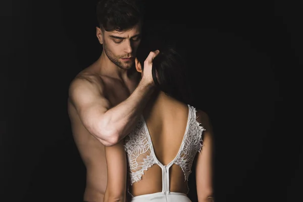 Handsome shirtless man hugging sexy girlfriend in white lingerie isolated on black — Stock Photo