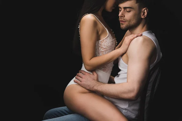 Vue partielle de la femme en lingerie blanche assise sur les genoux d'un bel homme isolé sur noir — Photo de stock