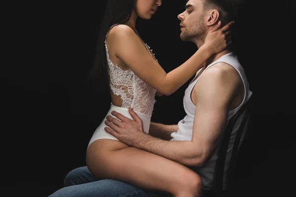 Cropped view of woman in white lingerie sitting on knees of handsome man isolated on black — Stock Photo